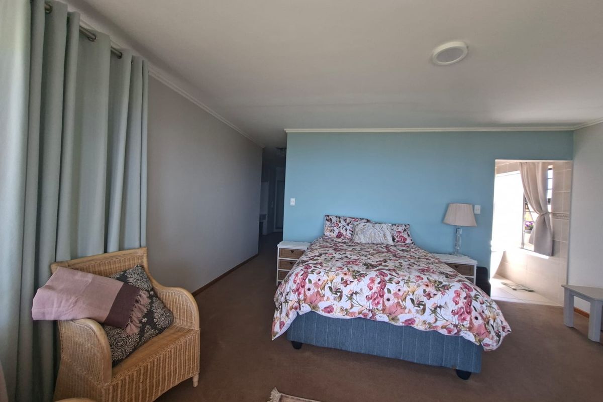 Spacious bedroom featuring neutral carpeting, a blue accent wall, and an adjoining en-suite bathroom area.