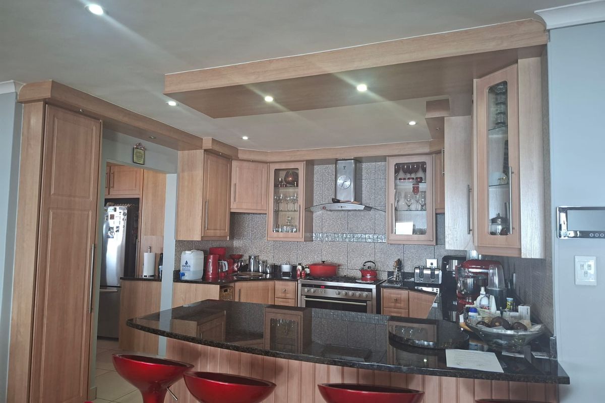 A well-appointed kitchen featuring light wood cabinetry, granite countertops, a breakfast bar, and a stainless steel gas stove with an extractor fan.