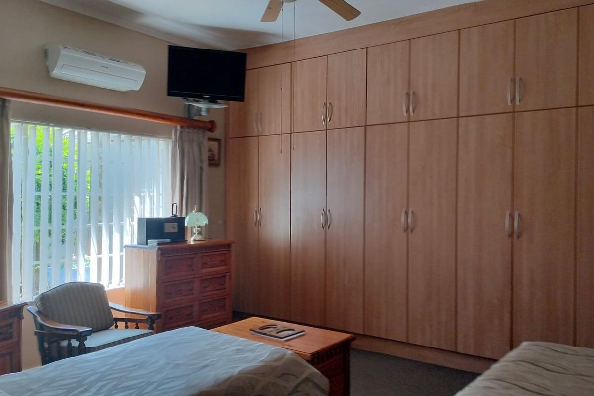 A bedroom featuring extensive floor-to-ceiling built-in wooden cabinetry, a wall-mounted air conditioning unit, and vertical window blinds.