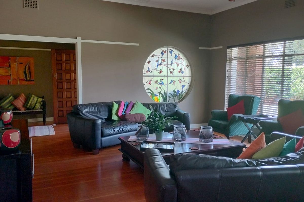 Spacious living room featuring polished timber flooring, a distinctive circular stained-glass window, and large windows with fitted blinds.
