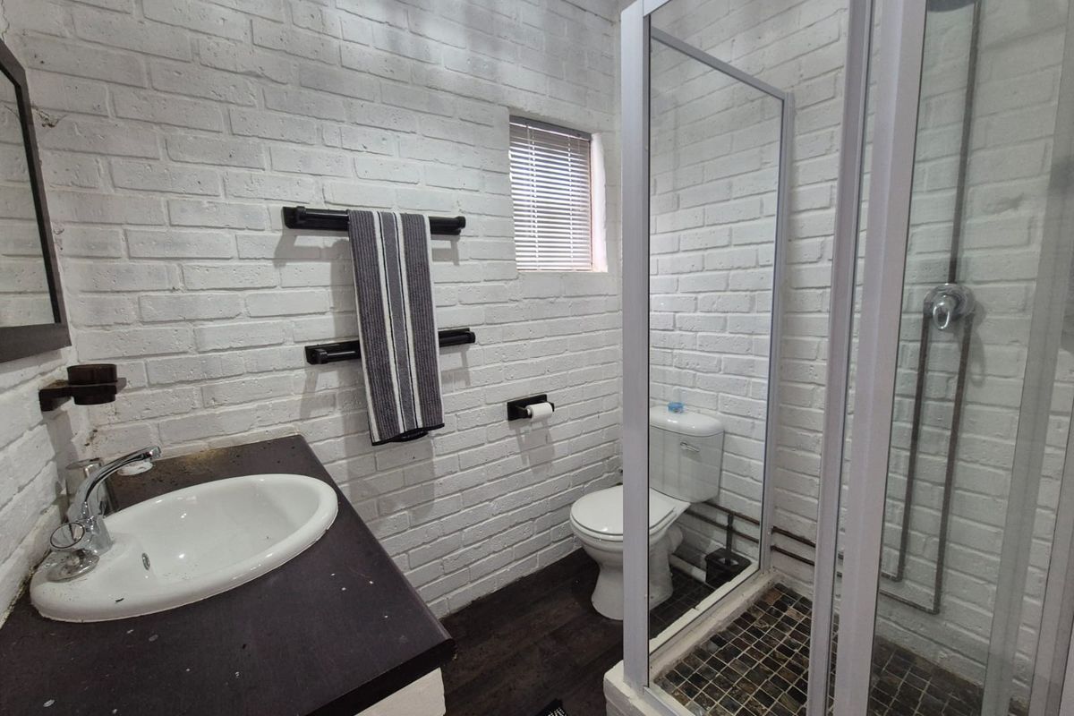 A compact bathroom featuring a white brick-style wall finish, a glass-enclosed shower, a vanity with a basin, and a toilet.