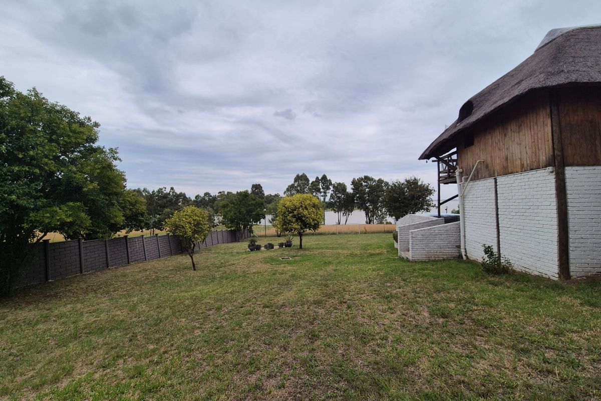 A spacious rear garden featuring a large lawn, perimeter boundary wall, and a view of the side elevation of the thatched-roof house.