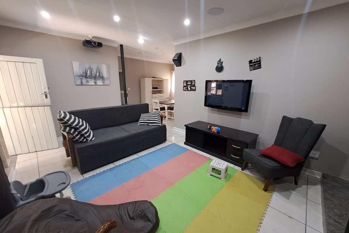 A spacious living room featuring tiled flooring, recessed ceiling lighting, and a wall-mounted television setup, with an open-plan layout leading to the dining area.