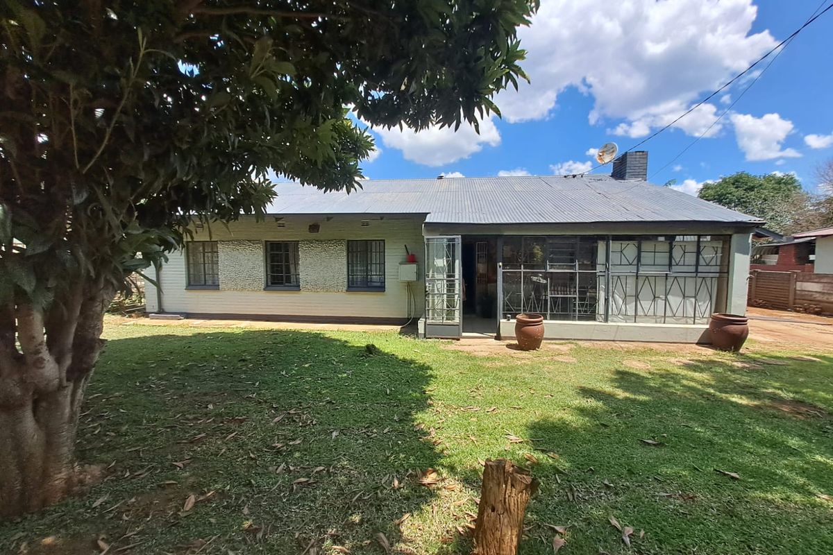 Rear view of a single-story house featuring a corrugated metal roof, brick and stone facade, and a covered patio area overlooking the garden.