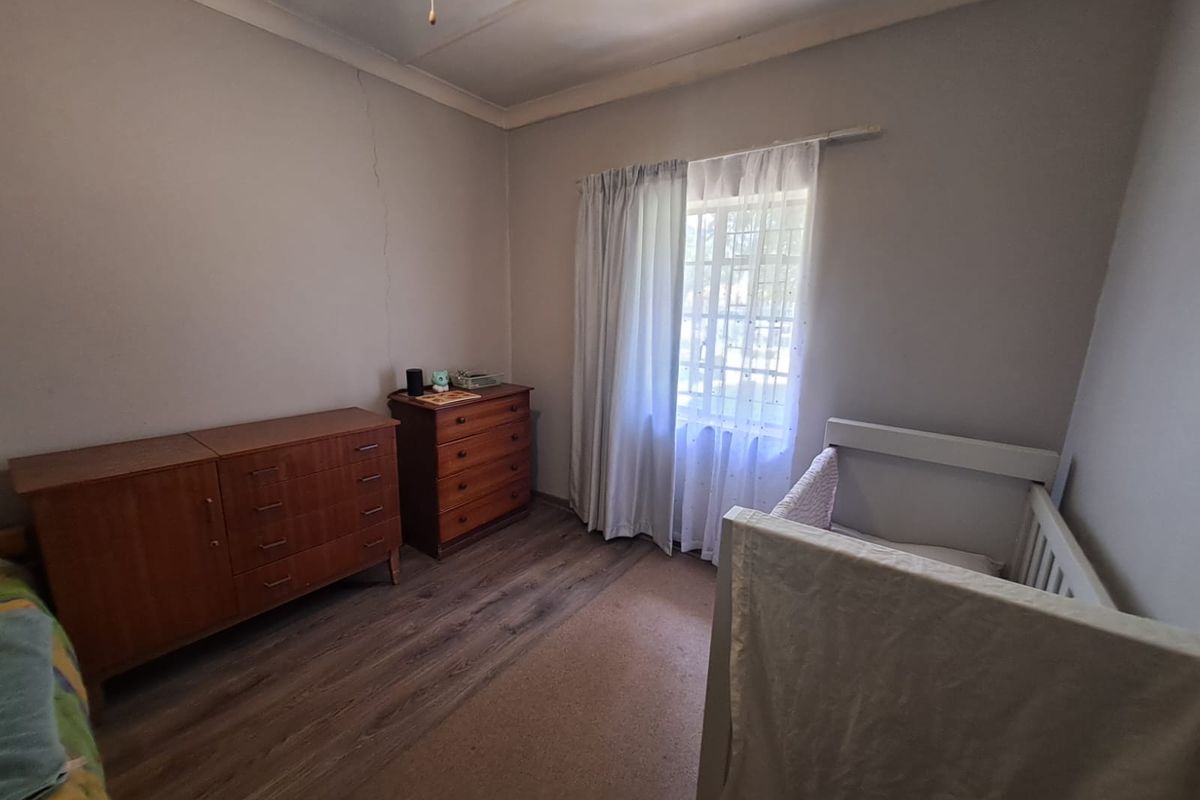 A bedroom featuring laminate flooring, a window with curtains, and visible wall cracking requiring maintenance.