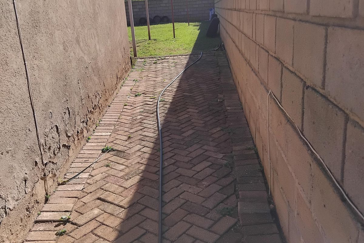 A narrow side passage featuring herringbone brick paving, bordered by a boundary wall and the side elevation of the house.