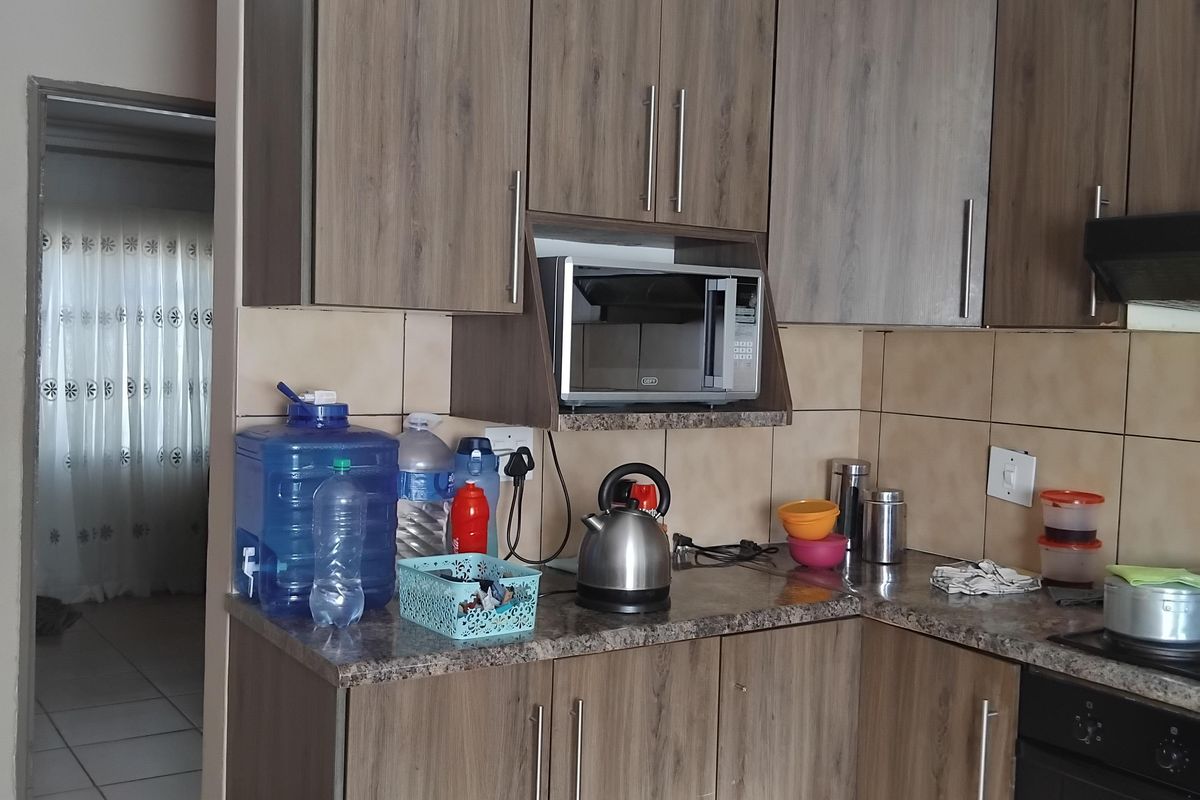 A functional kitchen featuring wood-look cabinetry, tiled splashbacks, built-in oven, and extractor fan, with tiled flooring throughout.