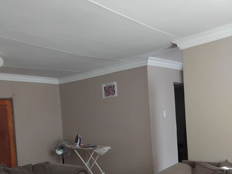 A living room featuring tiled flooring, decorative ceiling cornices, and neutral wall tones, providing a functional and open living space.