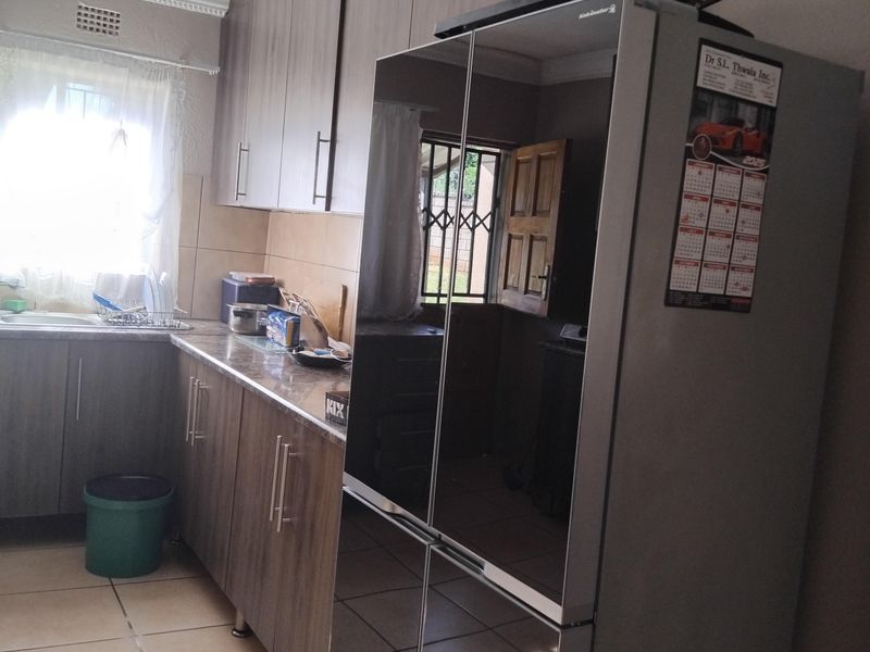 A functional kitchen featuring wood-grain cabinetry, tiled flooring, and a stainless steel sink, offering a practical layout for daily meal preparation.