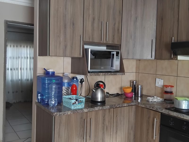 A functional kitchen featuring wood-look cabinetry, tiled splashbacks, built-in oven, and extractor fan, with tiled flooring throughout.