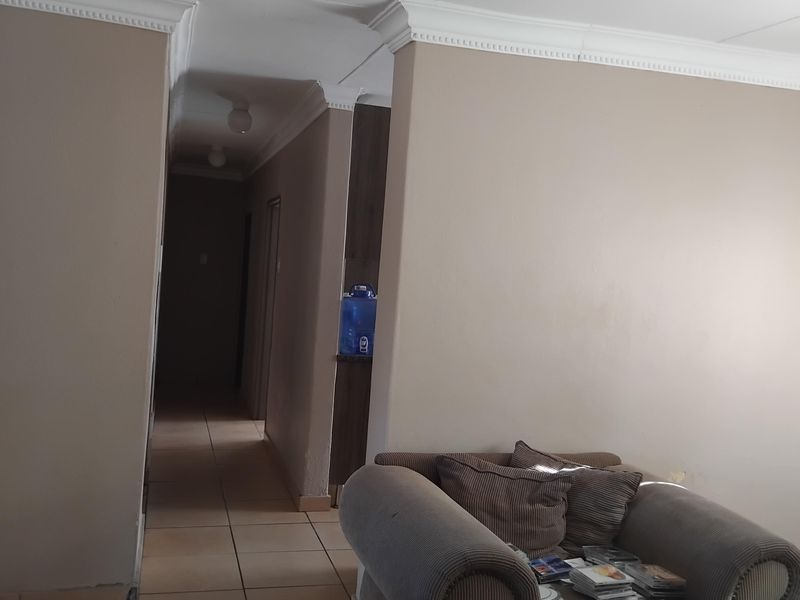 A view of a living area leading into a hallway, featuring neutral wall tones, decorative crown molding, and tiled flooring throughout.