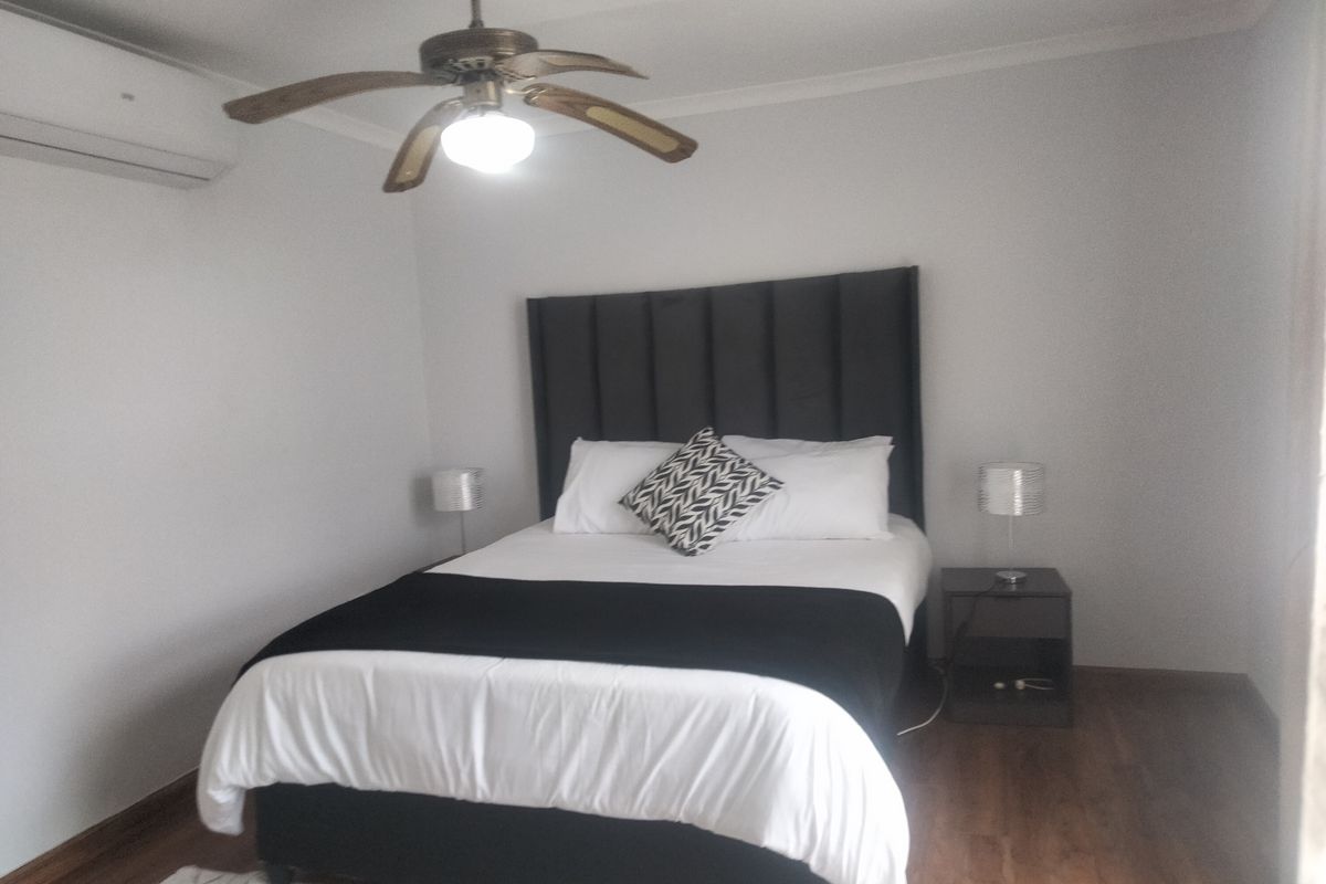A well-maintained bedroom featuring wood-look flooring, a ceiling fan, and a wall-mounted air conditioning unit.