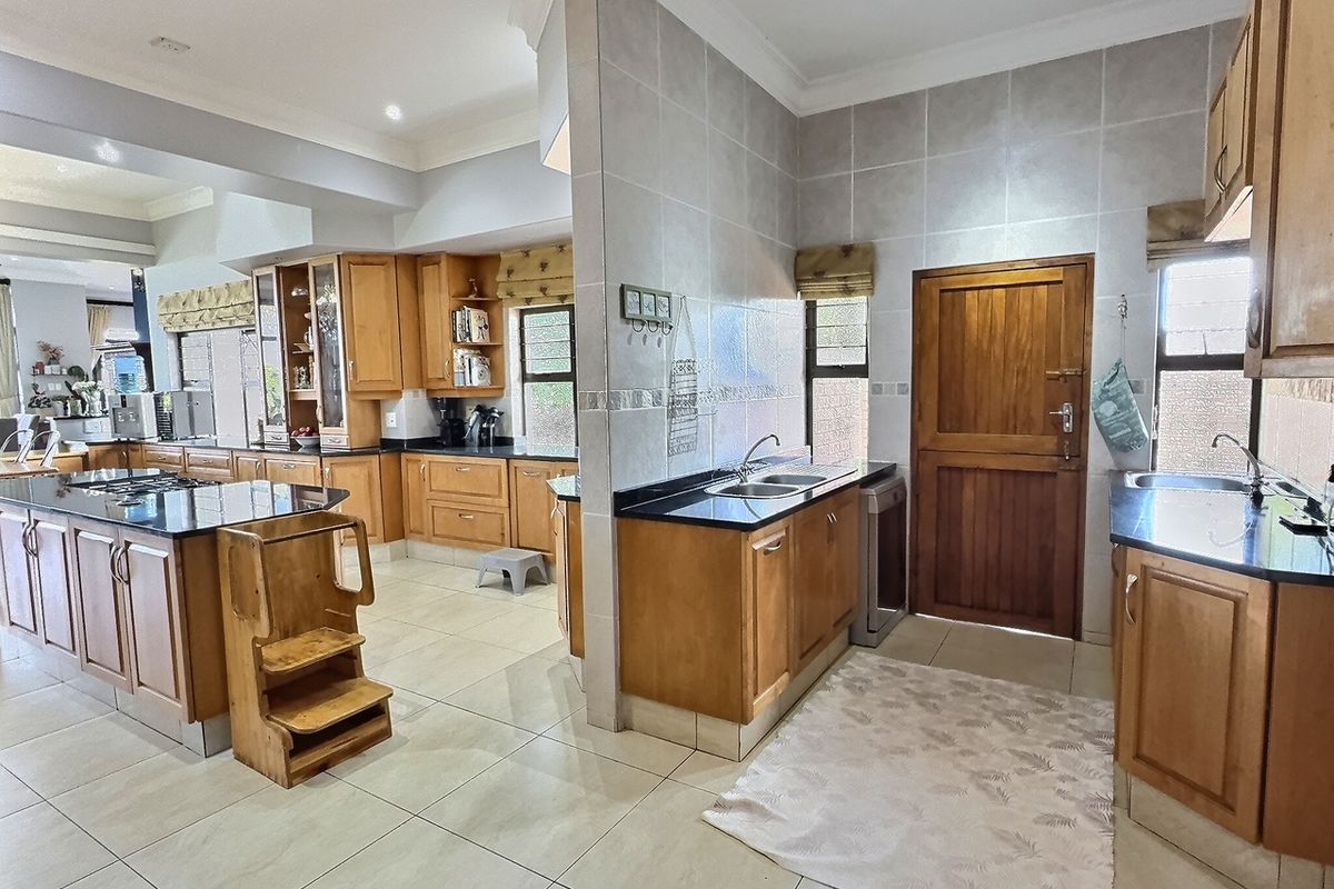 Spacious kitchen featuring wooden cabinetry, granite countertops, a central island with a built-in hob, and tiled flooring throughout.