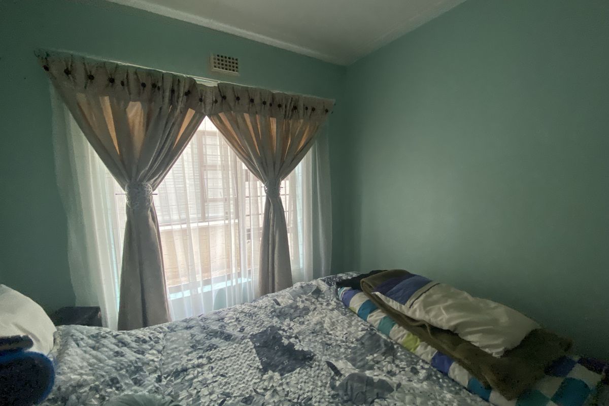 A standard bedroom featuring a large window with natural light, painted walls, and a ceiling ventilation vent.