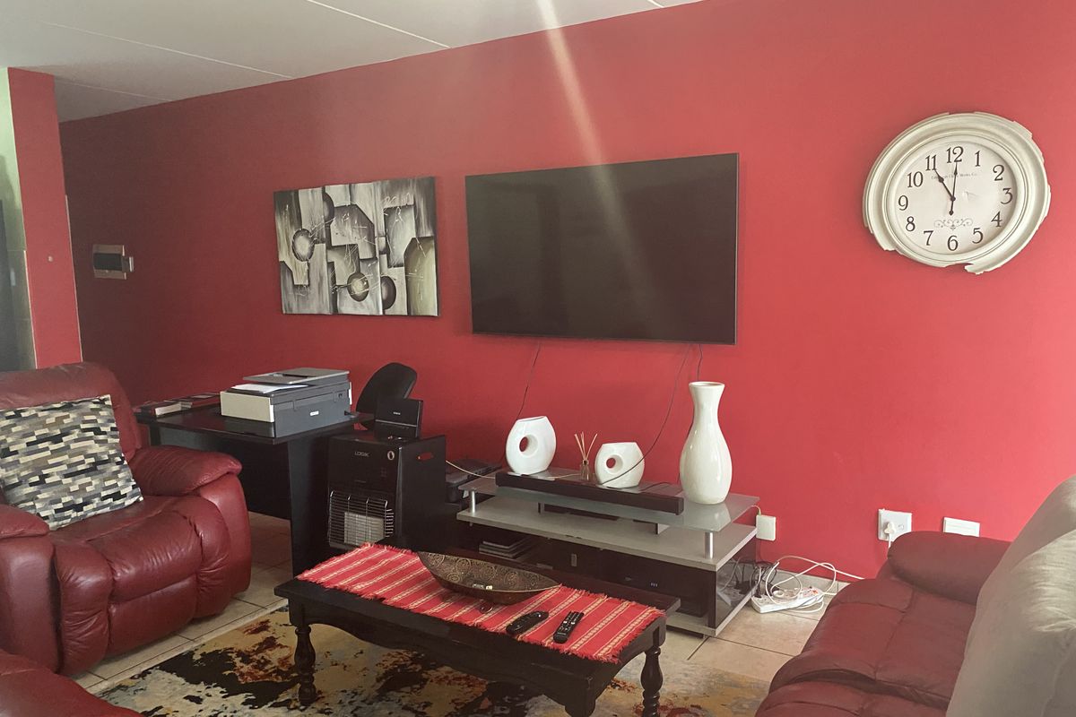 A living room featuring a prominent red accent wall, tiled flooring, and wall-mounted television setup.