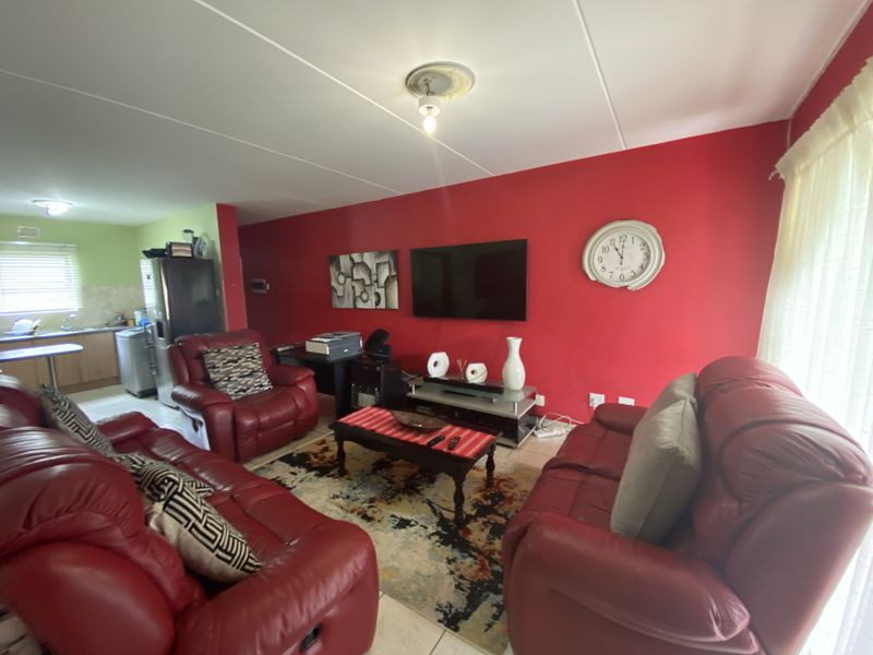 Open plan living area featuring a bright red accent wall, tiled flooring, and a seamless transition into the adjacent kitchen space.