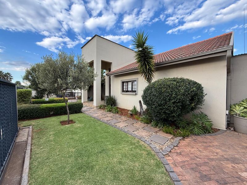 A well-maintained exterior view of the house featuring a paved walkway, manicured lawn, and established garden landscaping.