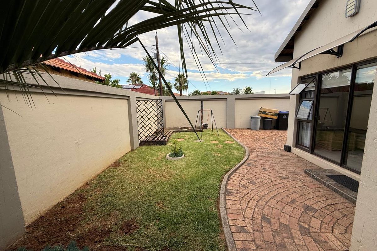 A private rear garden featuring a paved walkway, a small lawn area, and high perimeter boundary walls for added privacy.