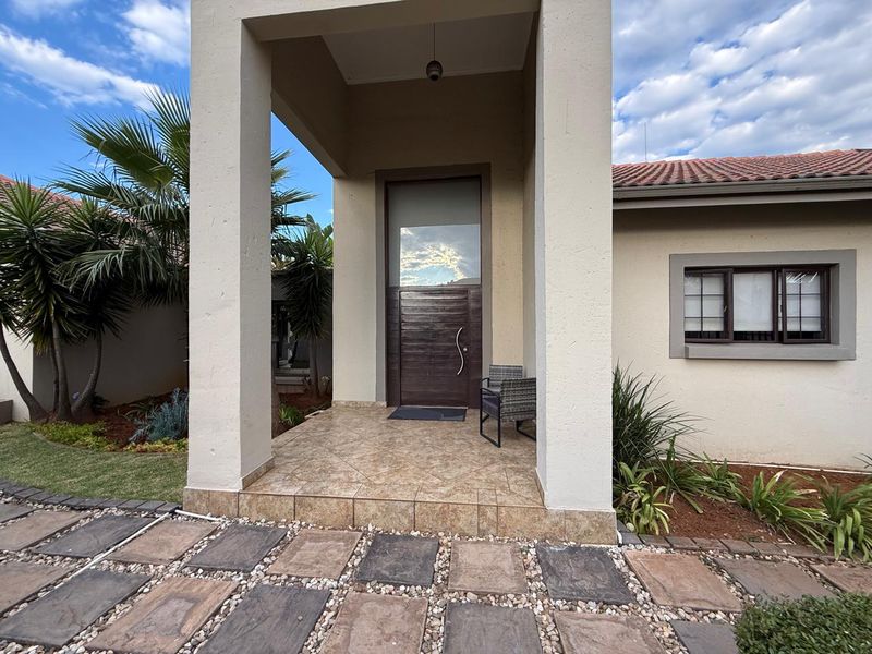 A welcoming front entrance featuring a covered porch with tiled flooring, a modern dark wood front door, and landscaped garden surrounds.