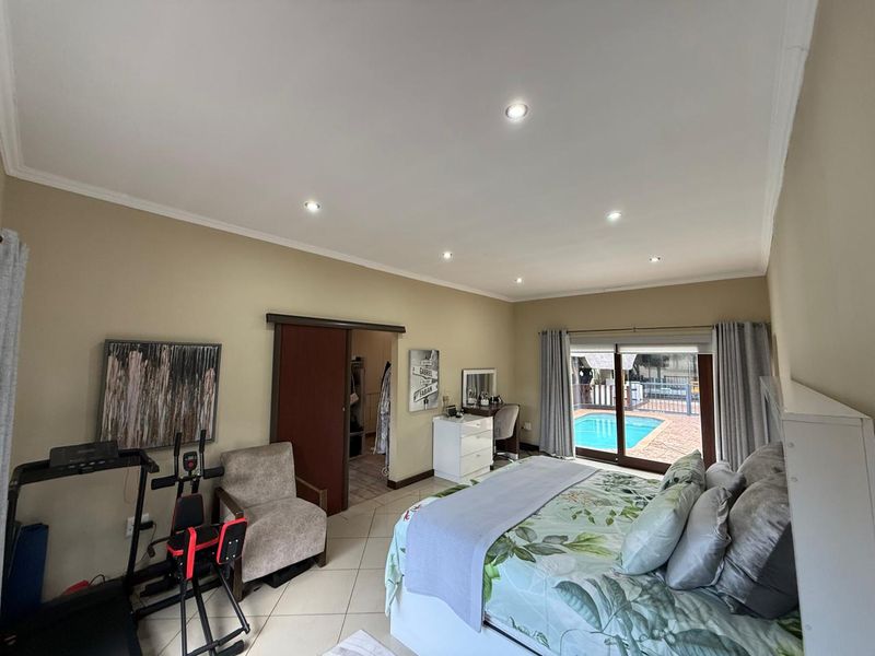 Spacious bedroom featuring tiled flooring, recessed downlighting, and sliding glass doors providing direct access to the outdoor pool area.