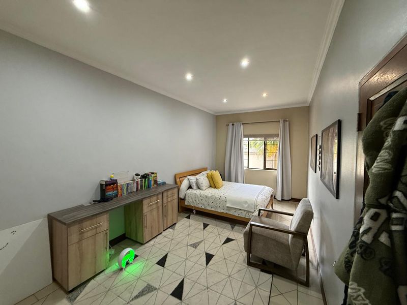A well-lit bedroom featuring tiled flooring, recessed ceiling lighting, and a window with curtain rails.