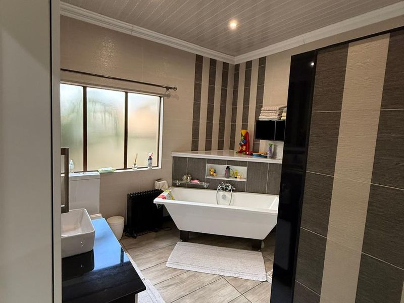 A bathroom featuring a freestanding bathtub, a vanity with a basin, tiled flooring, and a panelled ceiling with recessed lighting.