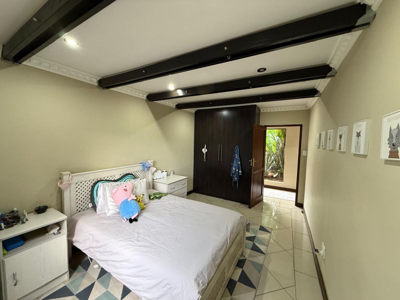 A bedroom featuring exposed dark timber ceiling beams, tiled flooring, and built-in dark wood cabinetry, with direct access to an outdoor area.