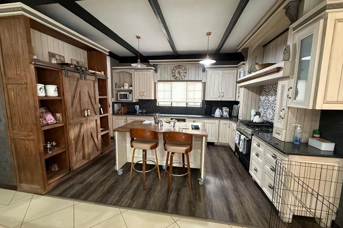 A rustic-style kitchen featuring custom cabinetry, a central island, dark wood-look flooring, and exposed ceiling beams.