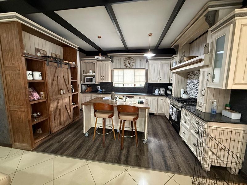 A rustic-style kitchen featuring custom cabinetry, a central island, dark wood-look flooring, and exposed ceiling beams.