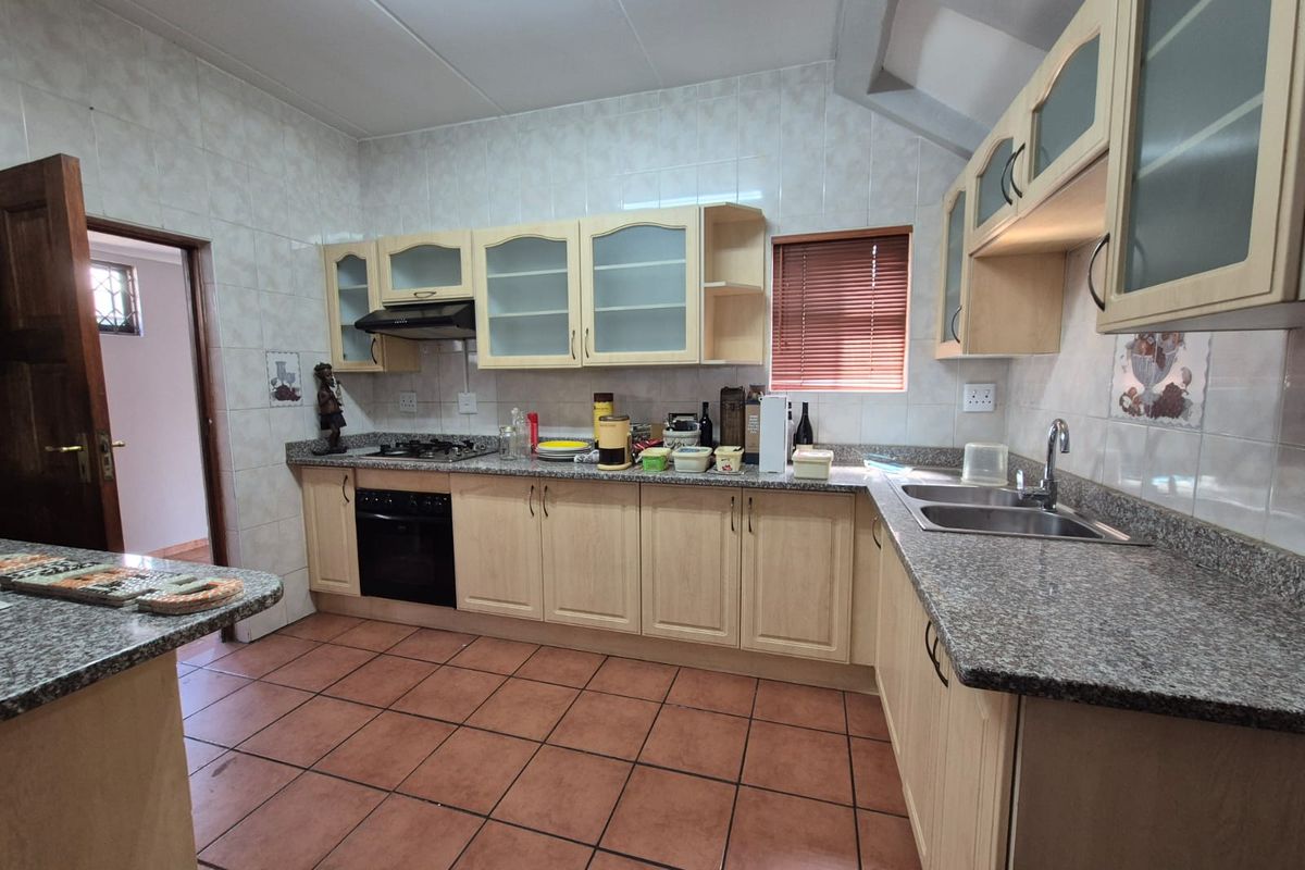 A functional kitchen featuring light wood cabinetry, granite-look countertops, a built-in oven with extractor fan, and tiled flooring throughout.