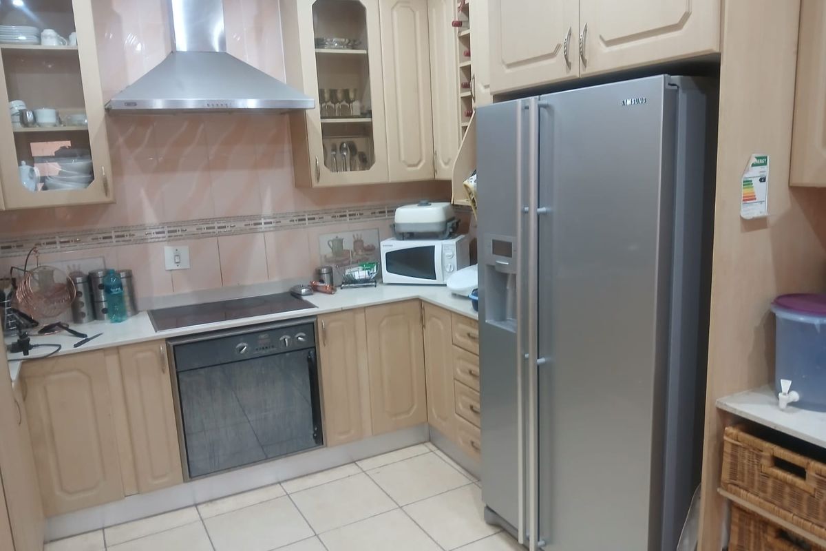 A functional kitchen featuring light wood cabinetry, a built-in oven, electric hob, stainless steel extractor fan, and tiled flooring.