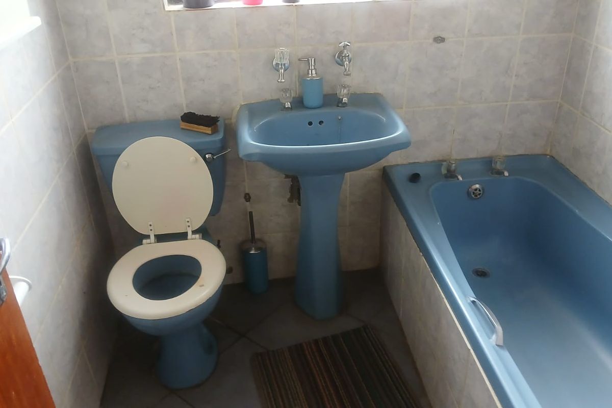 A dated bathroom featuring a blue pedestal basin, matching blue bathtub, and toilet, finished with light-colored wall tiling.