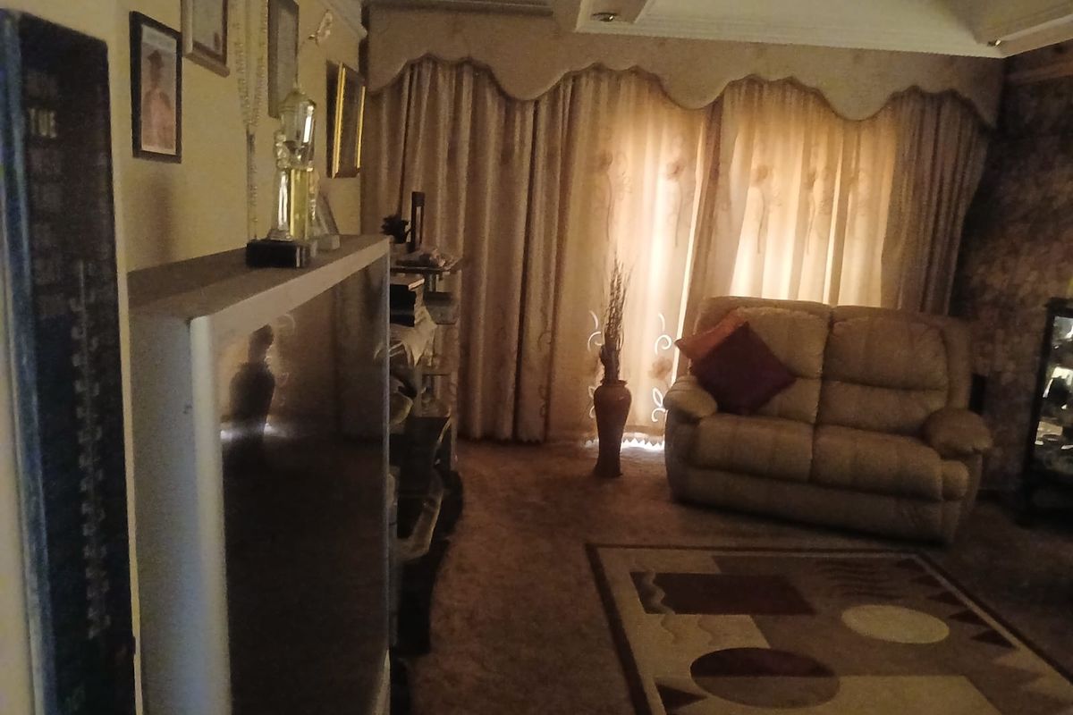 A cozy living room featuring a tray ceiling, carpeted flooring, and large window treatments, providing a comfortable and traditional living space.