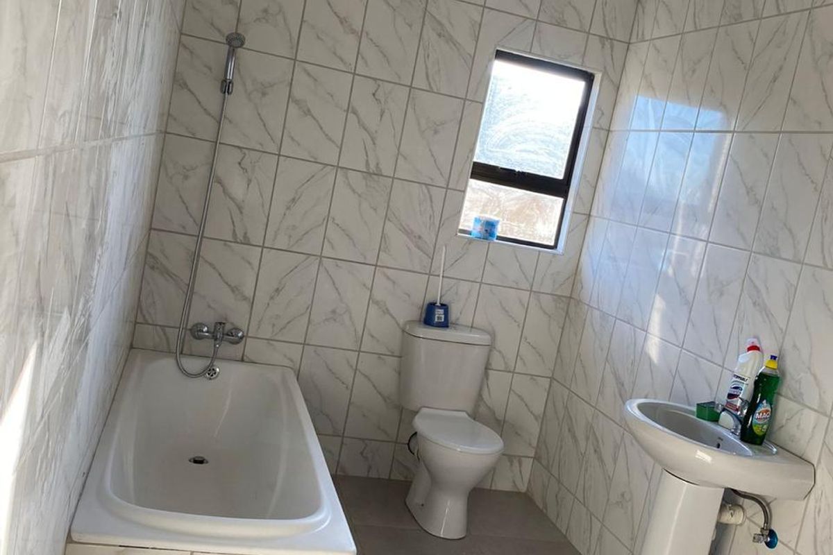 A functional bathroom featuring floor-to-ceiling marble-look wall tiles, a standard bathtub with shower attachment, a pedestal basin, and a toilet.