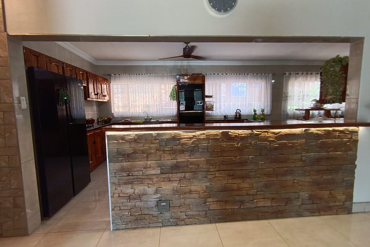 A functional kitchen featuring a stone-clad breakfast bar, wooden cabinetry, integrated oven, and tiled flooring, offering a warm and practical cooking space.