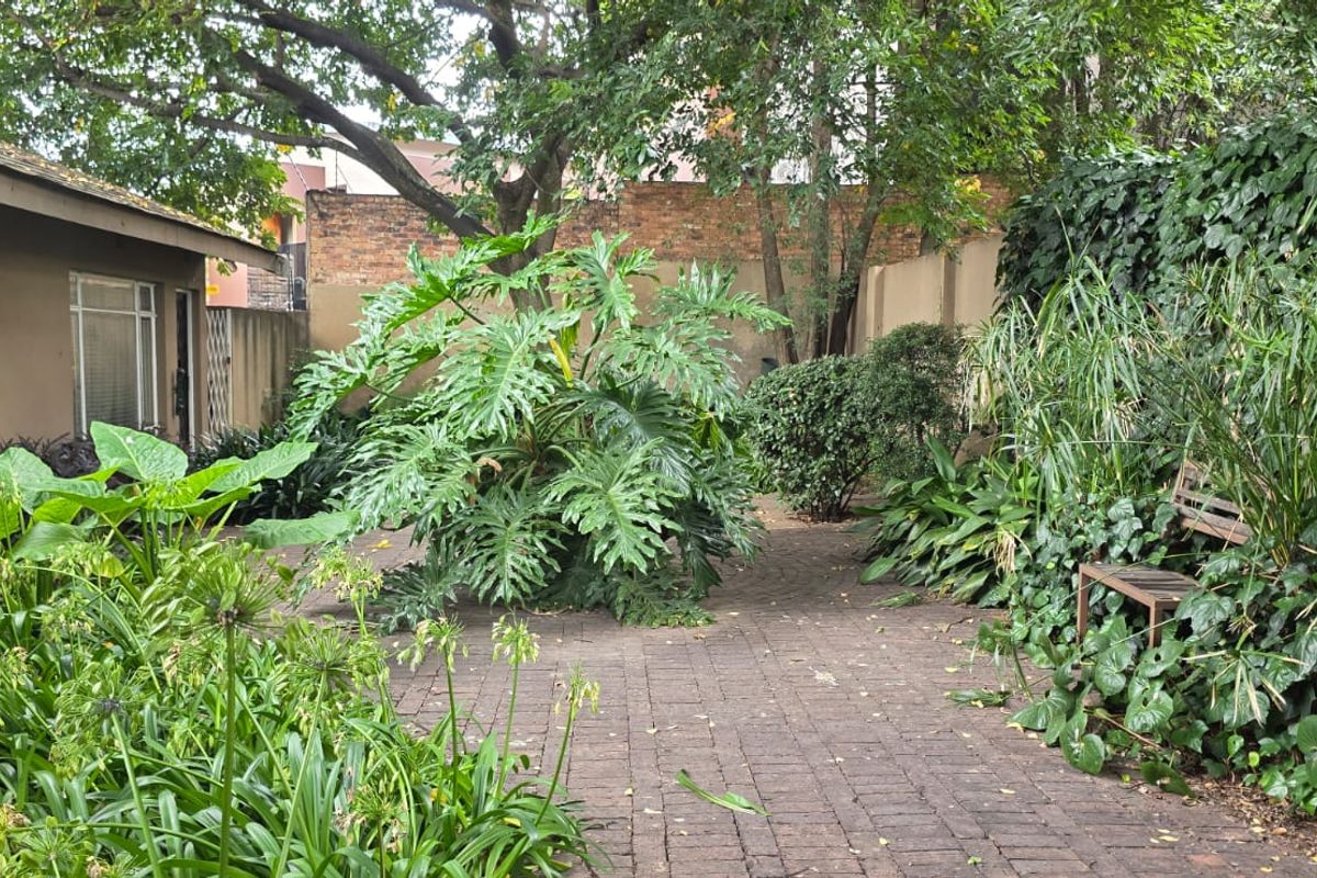 A private rear garden featuring established greenery, mature trees, and brick-paved pathways, offering a tranquil outdoor space adjacent to the main dwelling.