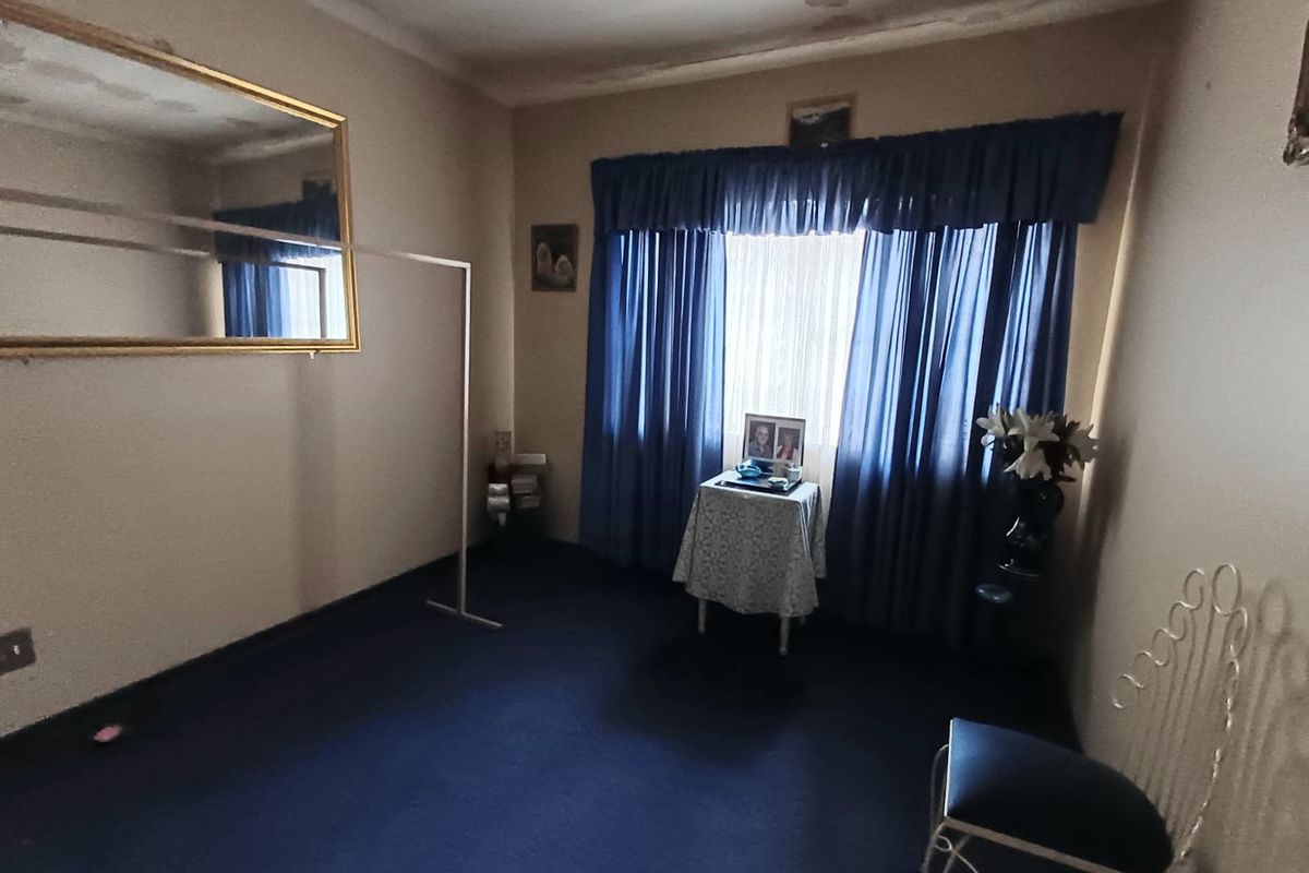 A bedroom featuring dark carpeting and a large wall-mounted mirror, currently showing signs of ceiling damage and wear.