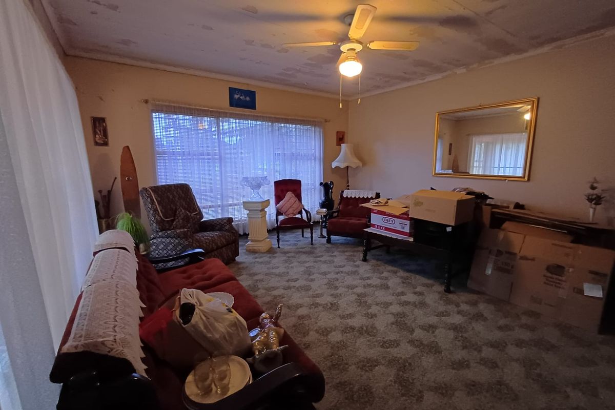 Spacious living room featuring a ceiling fan and large windows, currently requiring cosmetic updates to the ceiling and flooring.