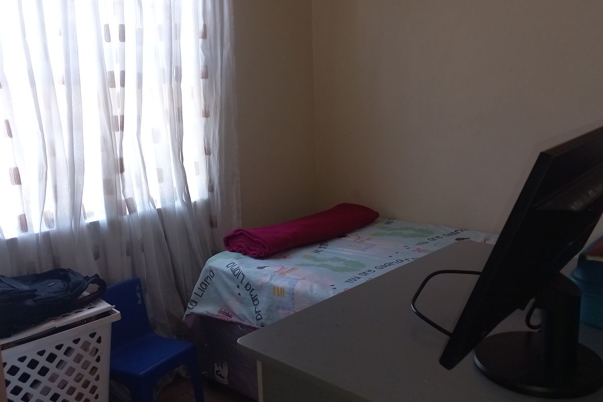 A compact bedroom featuring tiled flooring and a window with sheer curtains, providing natural light to the space.