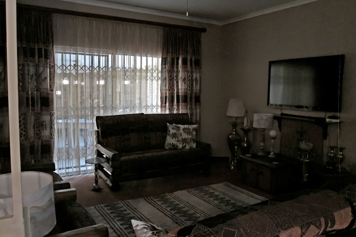 A dimly lit living room featuring a sliding glass door with security gate access to the exterior and a ceiling fan.