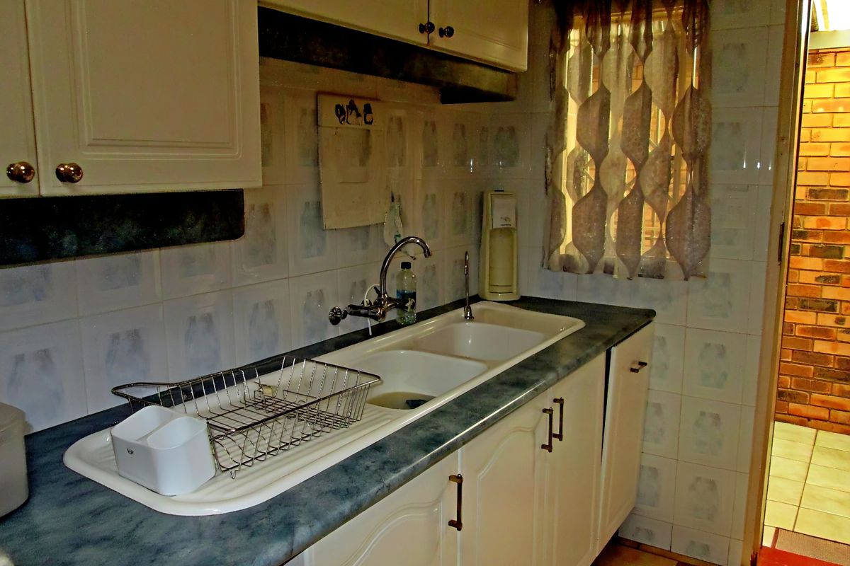 A functional kitchen scullery area featuring a double basin sink, laminate countertops, and tiled wall finishes, offering potential for a modern cosmetic update.