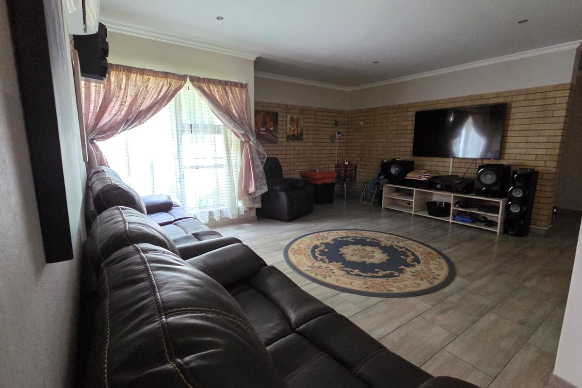 Spacious living room featuring tiled flooring, a prominent face-brick feature wall, and recessed ceiling lighting.