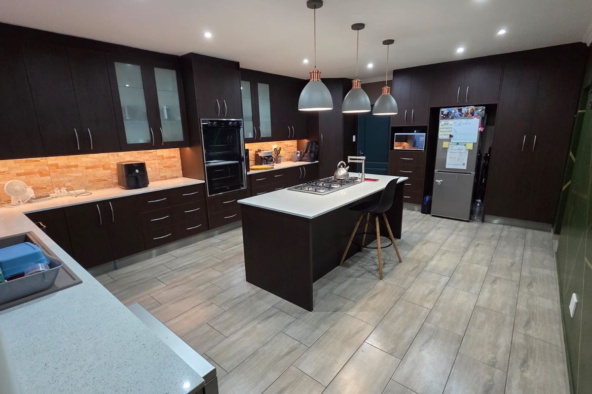 Modern kitchen featuring dark cabinetry, stone countertops, a central island with a gas hob, and integrated oven, complemented by tiled flooring and recessed lighting.