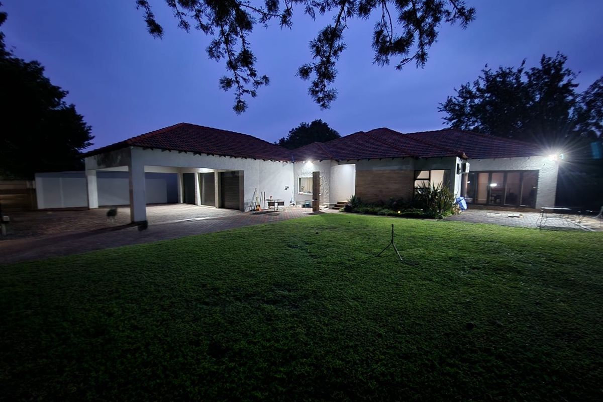 A twilight view of the rear exterior featuring a spacious lawn, paved driveway, and a covered carport area attached to the main house structure.