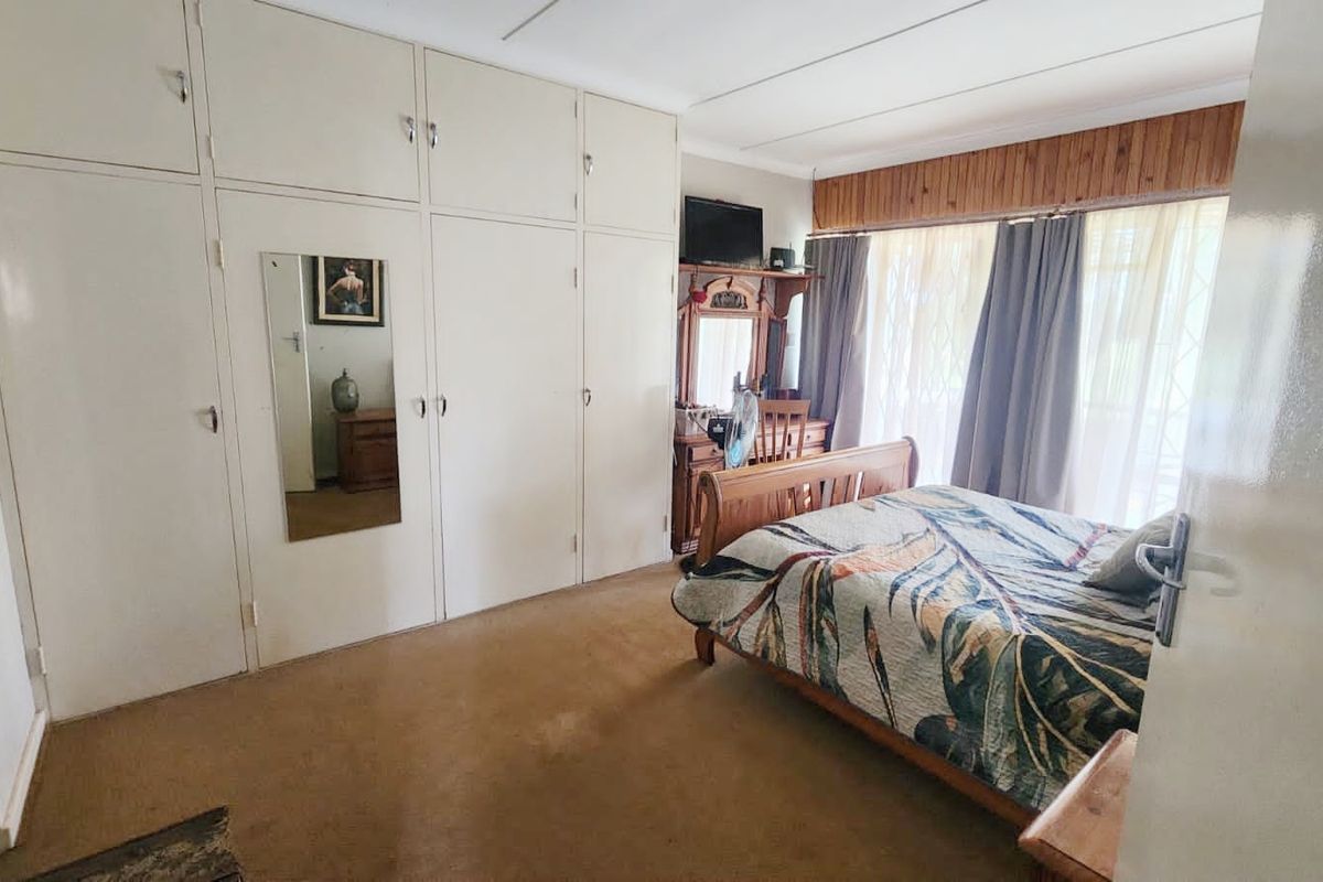 A bedroom featuring extensive built-in floor-to-ceiling cabinetry, carpeted flooring, and large windows with wood-paneled trim.