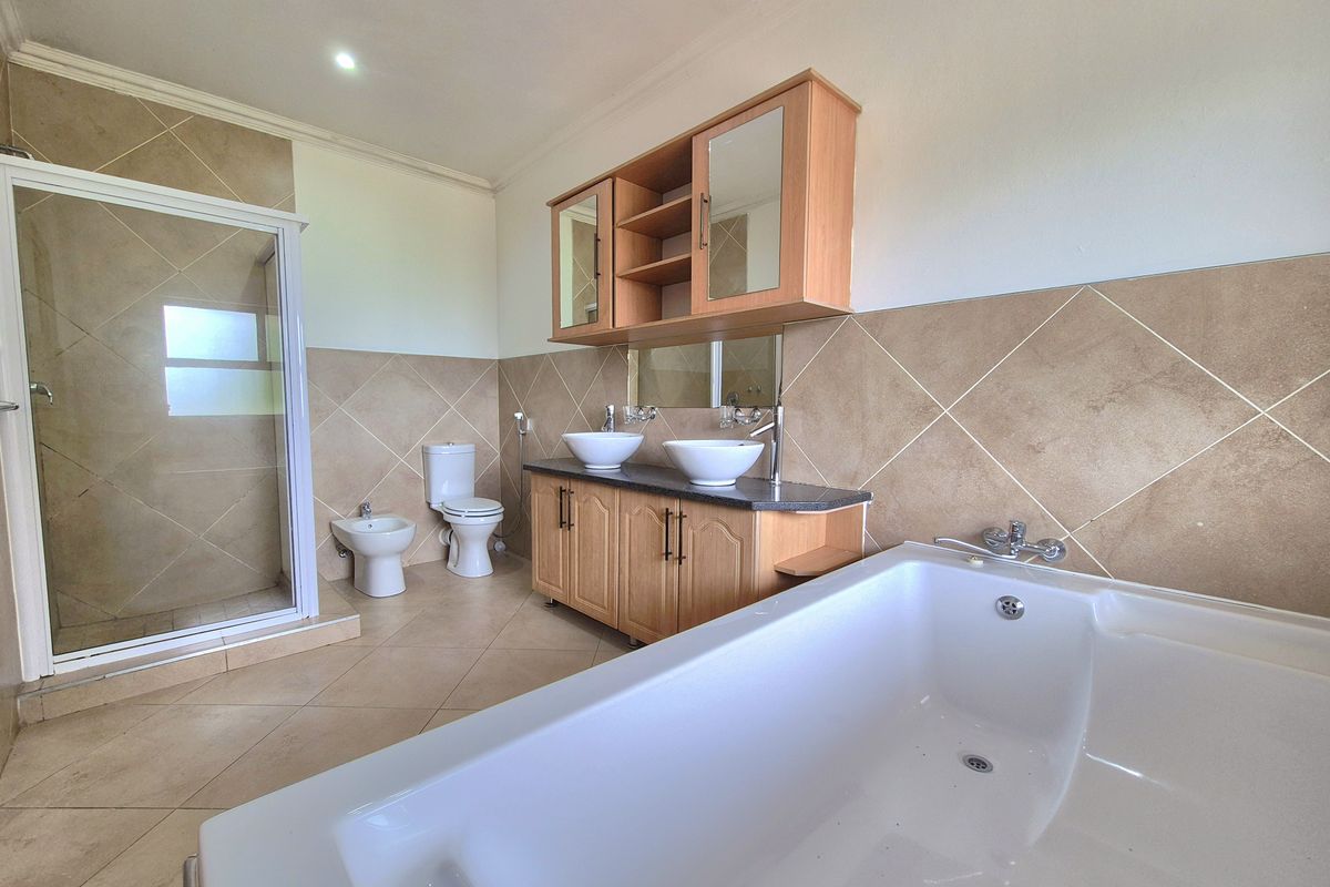 Spacious bathroom featuring a double vanity with vessel sinks, a separate glass-enclosed shower, a bathtub, a toilet, and a bidet with neutral tiling.