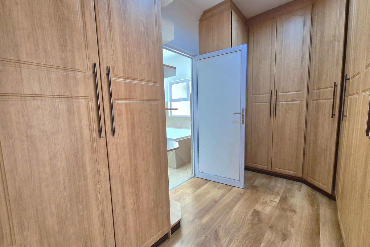 A walk-in dressing area featuring extensive built-in wooden cabinetry and laminate flooring, with direct access to an adjoining bathroom.