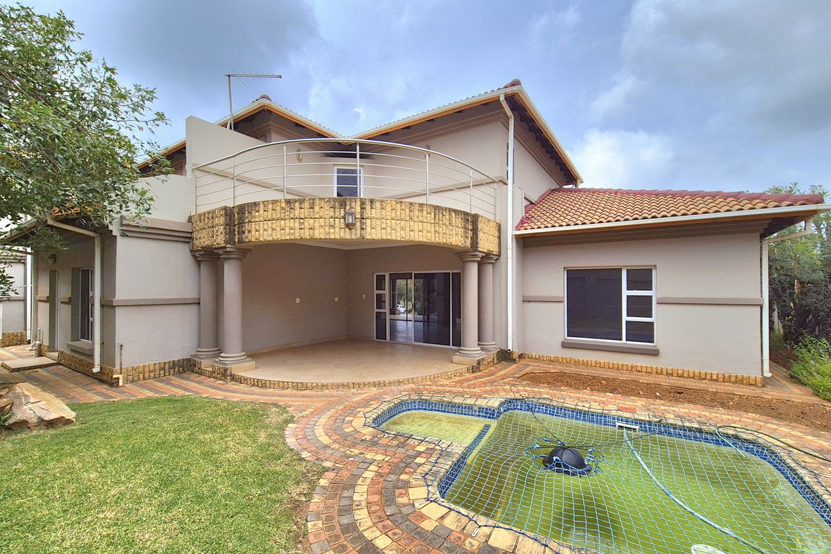 Rear view of the property featuring a covered patio, an upper-level balcony with metal railings, and a swimming pool with paved surround.