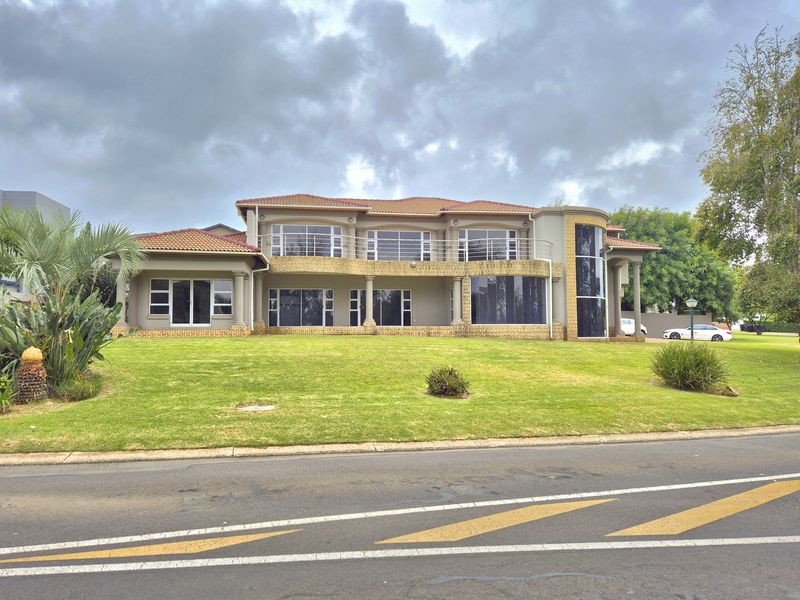 A spacious double-story residential property featuring a tiled roof, large glass windows, a balcony, and a well-maintained front lawn.