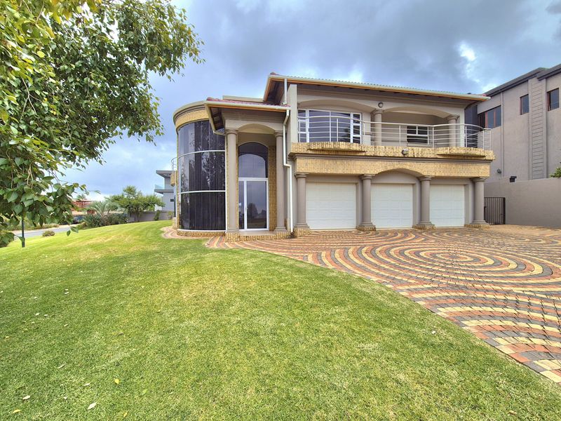 A grand double-story residence featuring a triple garage, curved glass facade, and a paved driveway set within a well-maintained garden.
